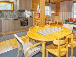 A modern kitchen with stainless steel appliances, a dining area with a round wooden table and chairs, and a living room with a sofa and chairs.