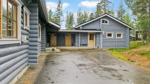 Une cabane en rondins avec un porche, une porte d’entrée et un petit jardin devant.