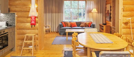 A cozy log cabin interior with a dining area, sofa, and kitchen.