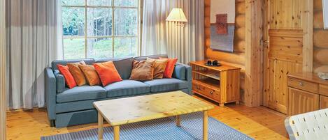 A cozy cabin interior with a sofa, a wooden table, and a view of the outdoors.