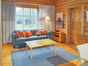 Interior acogedor de una cabaña con un sofá, una mesa de madera y vistas al exterior.