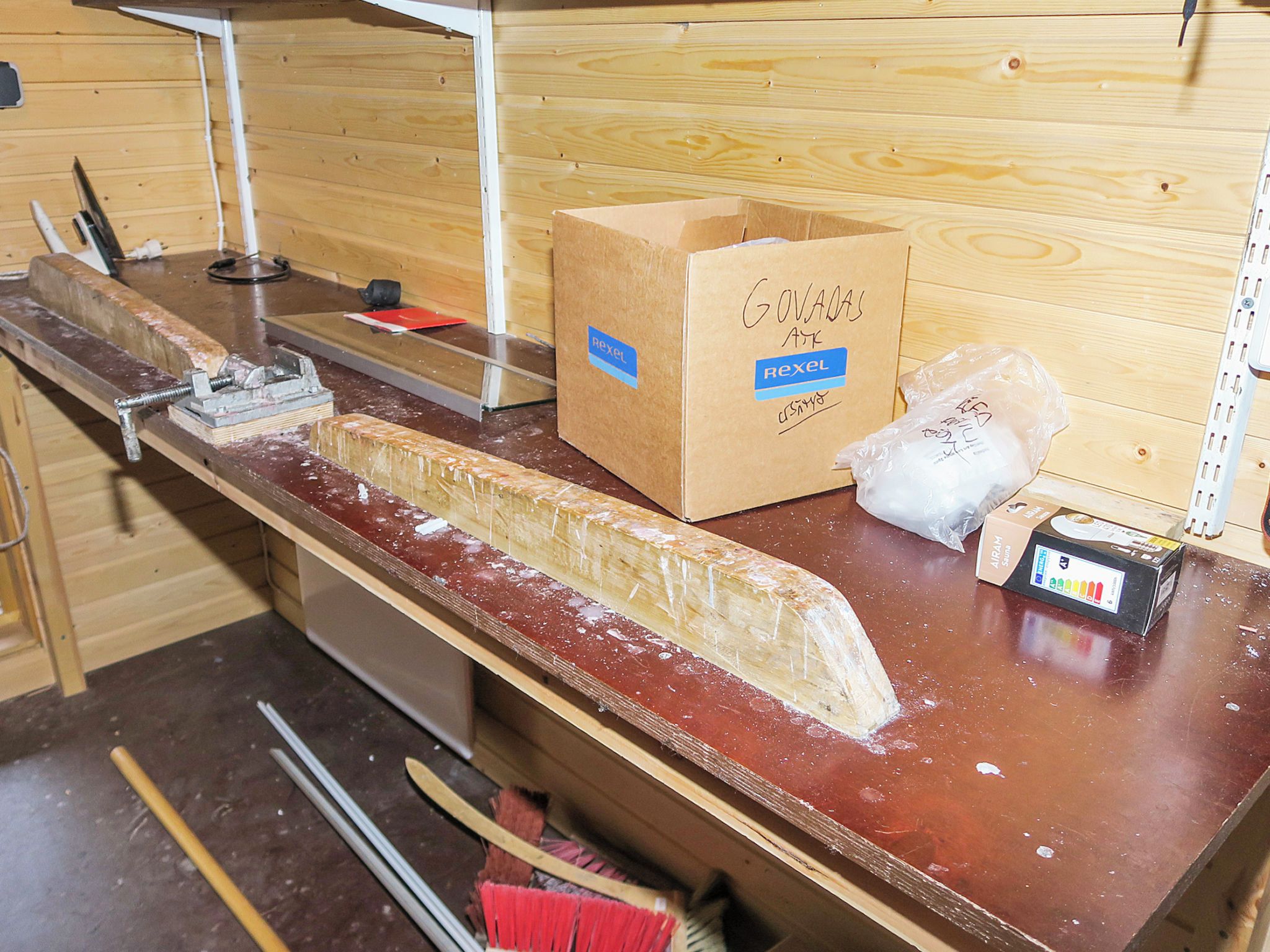 Un atelier avec un établi, une boîte en bois étiquetée « Rexel » et un sac en plastique posé sur le comptoir.