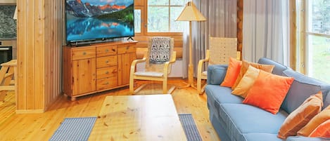 Interior acogedor de una cabaña con televisor, muebles de madera y una ventana con cortinas.