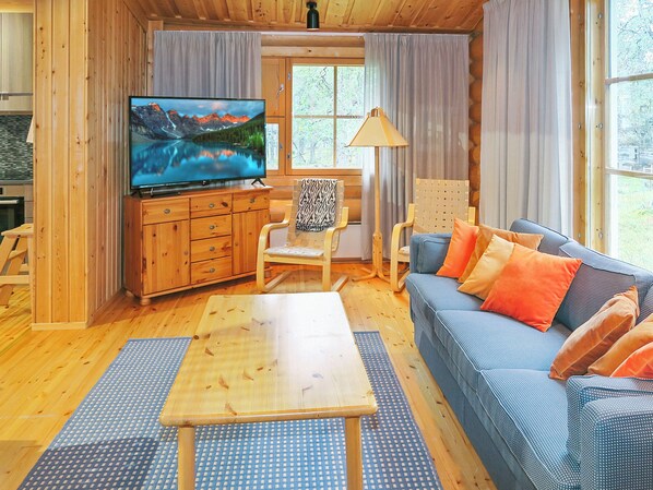 L’intérieur d’un chalet confortable, avec un téléviseur, des meubles en bois et une fenêtre agrémentée de rideaux.