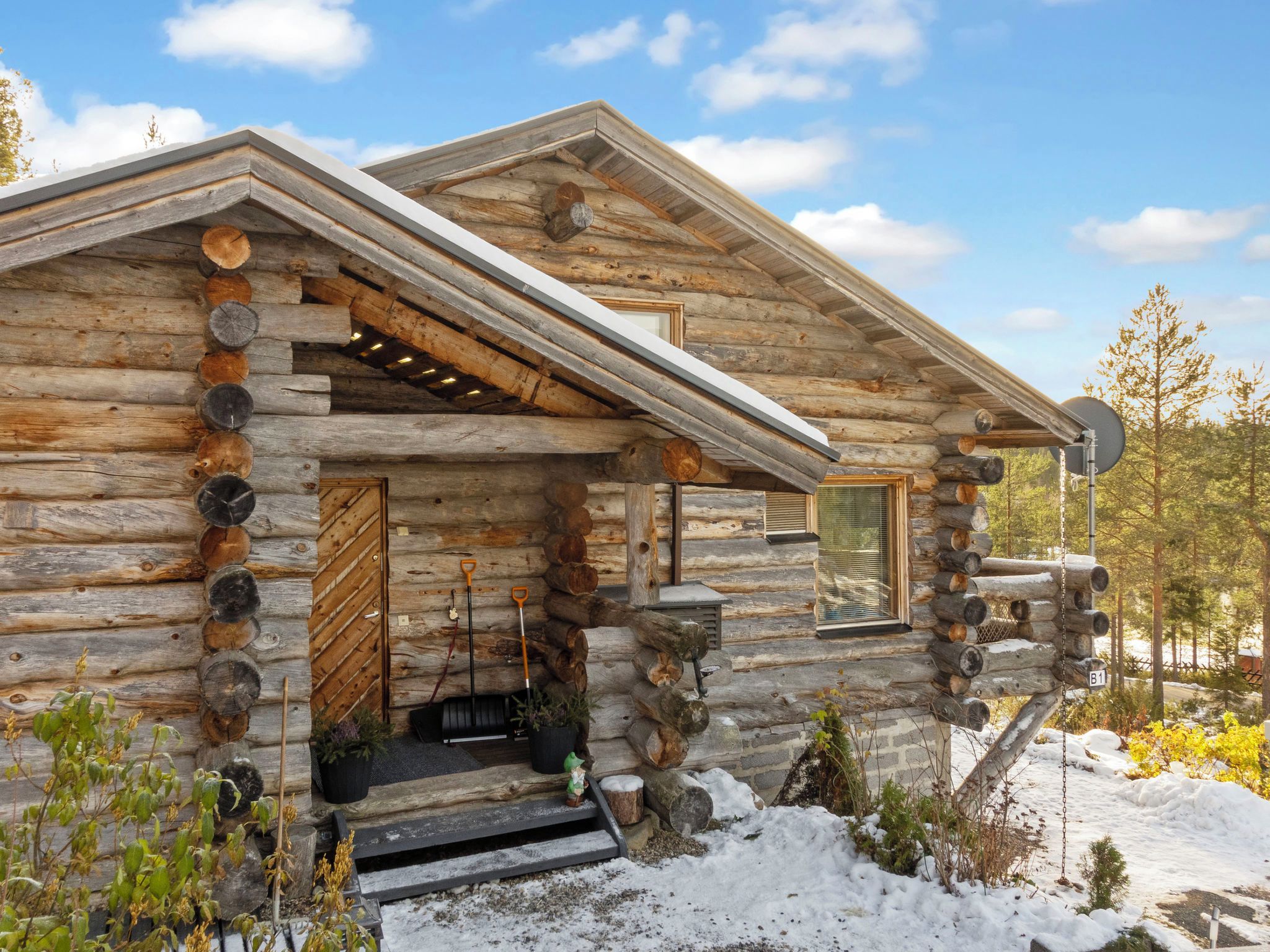 Une cabane en rondins, avec une façade en bois, un porche à l’avant et un sol recouvert de neige.