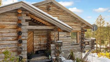 Une cabane en rondins, avec une façade en bois, un porche à l’avant et un sol recouvert de neige.