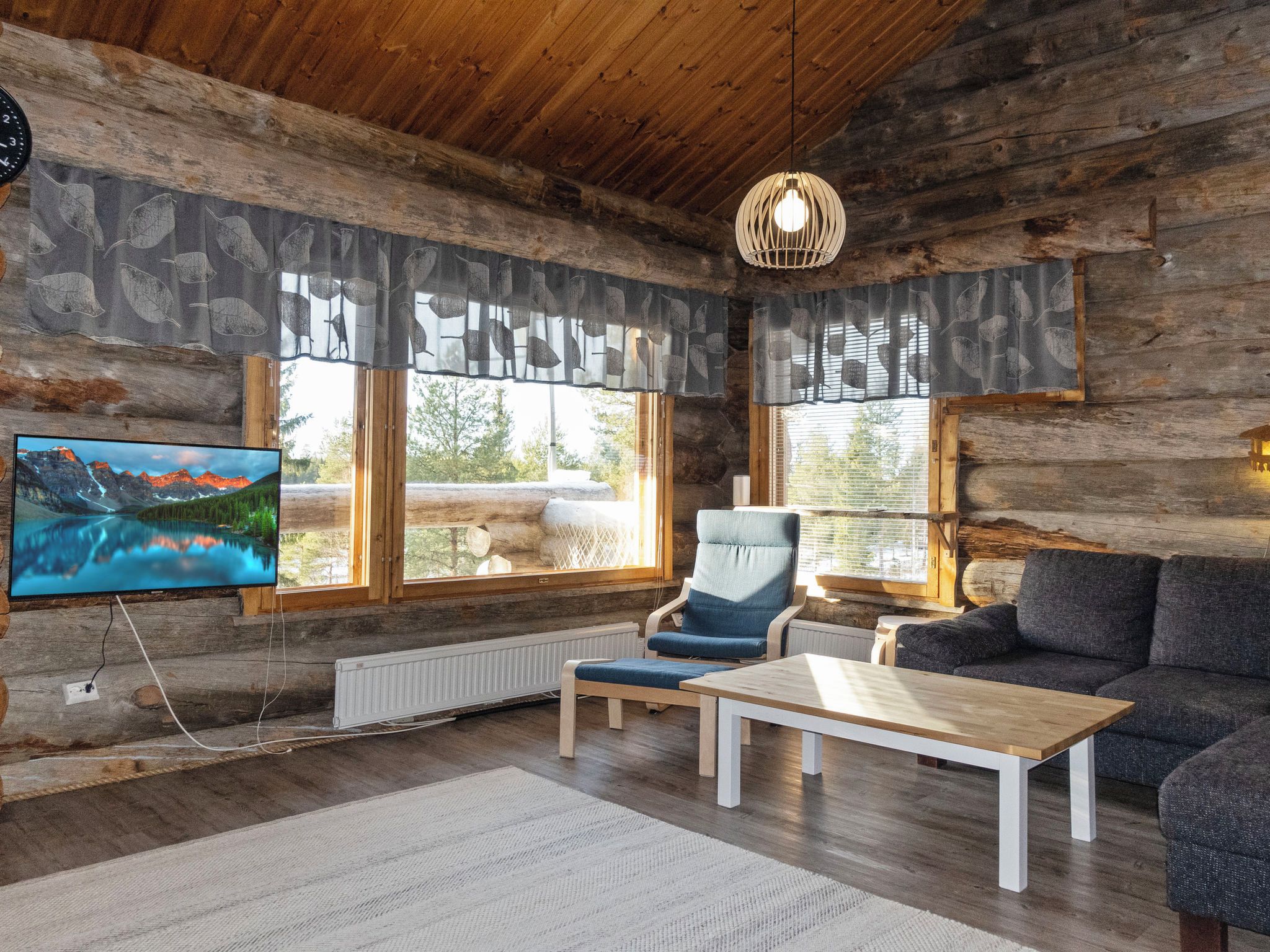 Ein Blockhaus-Interieur mit Fernseher, einer Couch, einem Sessel und einem Tisch.
