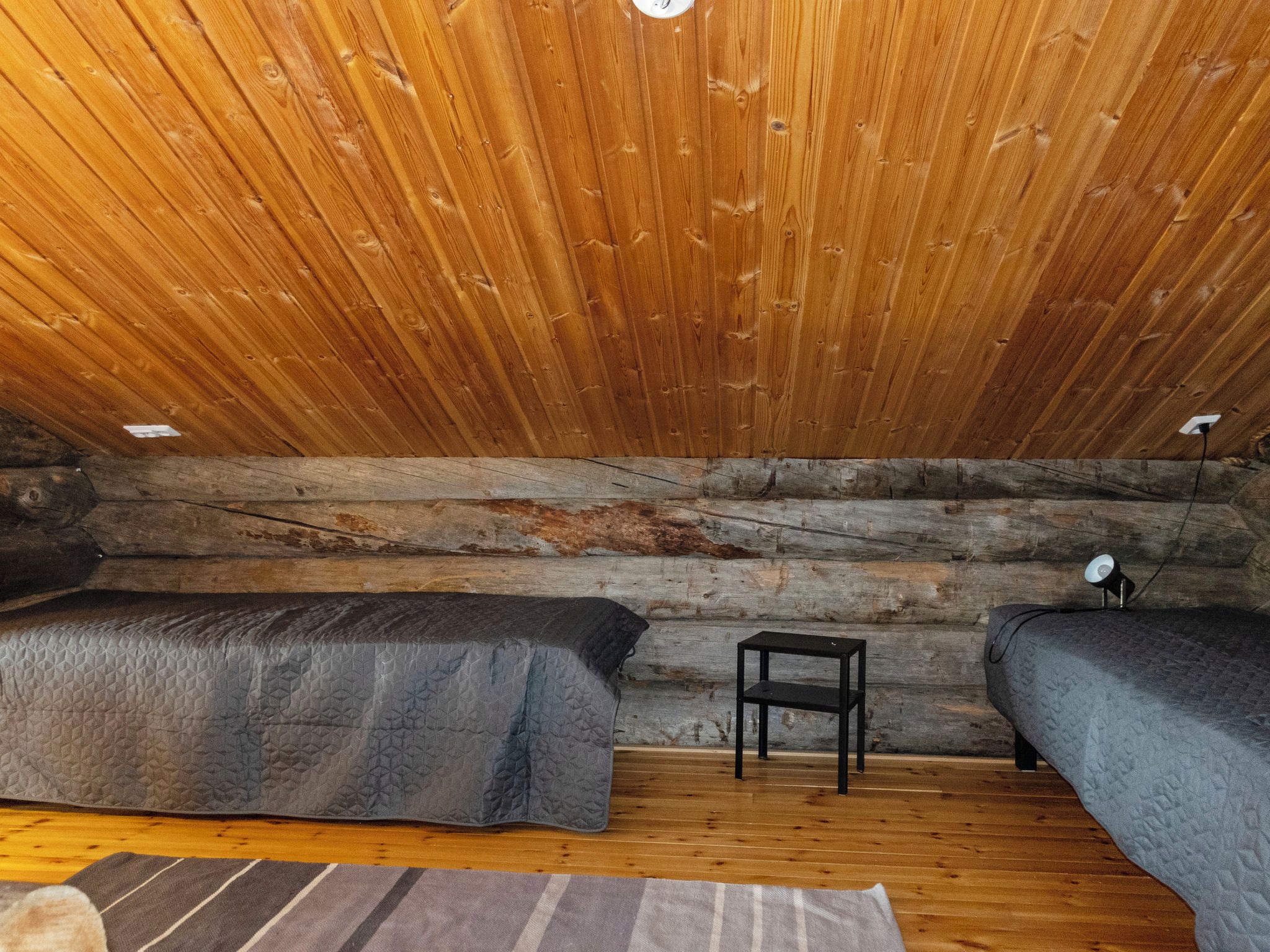 Une chambre dans un chalet en rondins, avec deux lits, une petite table et une lampe.