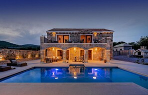 Une maison en pierre à deux étages avec une piscine devant.