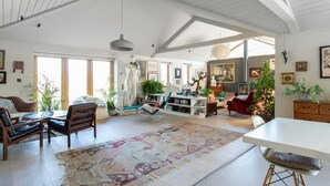 A spacious living room with a high ceiling, a large rug, and a dining area with a white table. - Luxury Countryside Haven for 10 (Chichester)