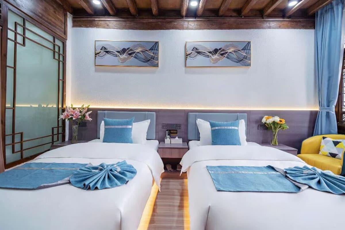 Ein Hotelzimmer mit zwei Betten, Holzboden, Kunstwerk an der Wand und einem Nachttisch mit einer Uhr.