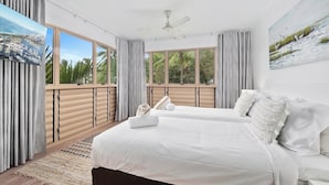 Un dormitorio moderno con una cama grande, ventilador de techo y ventanas amplias con cortinas.