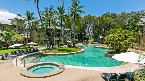 Zona de piscina en un resort con varias piscinas, sillones de descanso y palmeras.