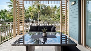Un balcón con una mesa de vidrio, un sofá negro y una planta en maceta.