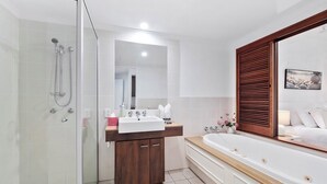 A modern bathroom with a glass shower enclosure, a wooden vanity, a large bathtub, and a mirror with a wooden frame. - Top Floor Studio Amphora (Cairns)