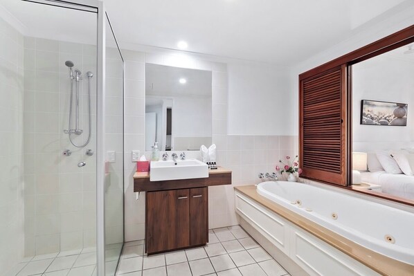A modern bathroom with a glass shower enclosure, a wooden vanity, a large bathtub, and a mirror with a wooden frame.