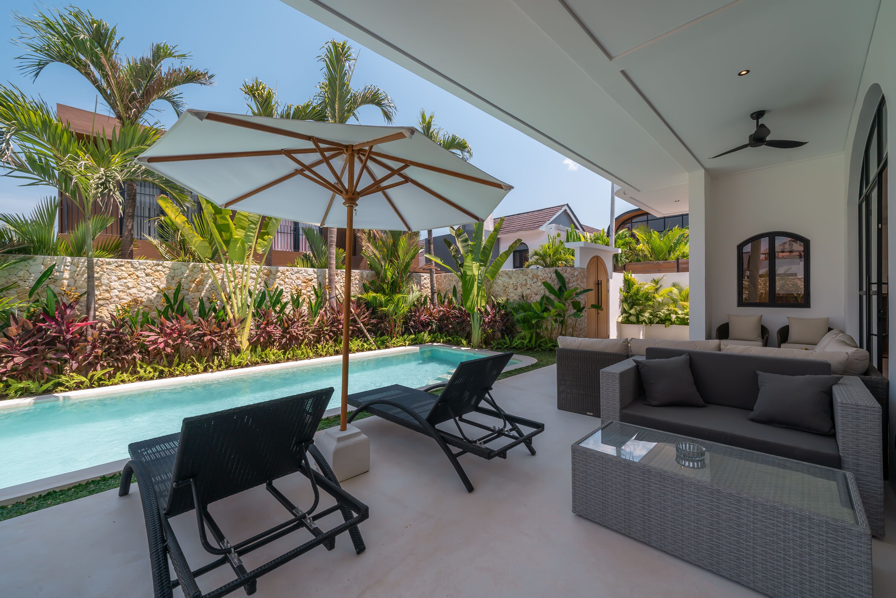 A poolside area with lounge chairs, a glass table, and a large umbrella.