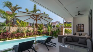 Ein Poolbereich mit Liegestühlen, einem Glastisch und einem großen Sonnenschirm.