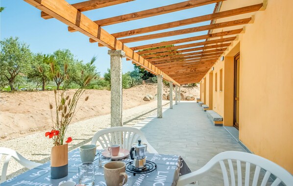 A covered outdoor seating area with a table set for two, chairs, and a coffee maker. - Awesome home in Badesi (OT) (Badesi (OT))