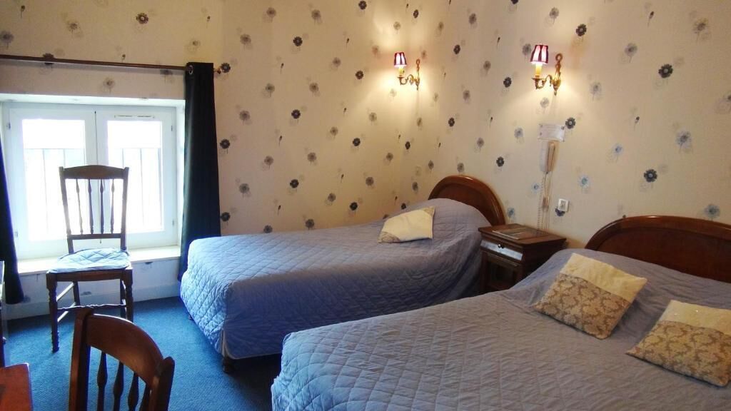 Ein Zimmer mit zwei Einzelbetten, einem Holzstuhl, einem Nachttisch und einem Fenster mit Vorhängen.
