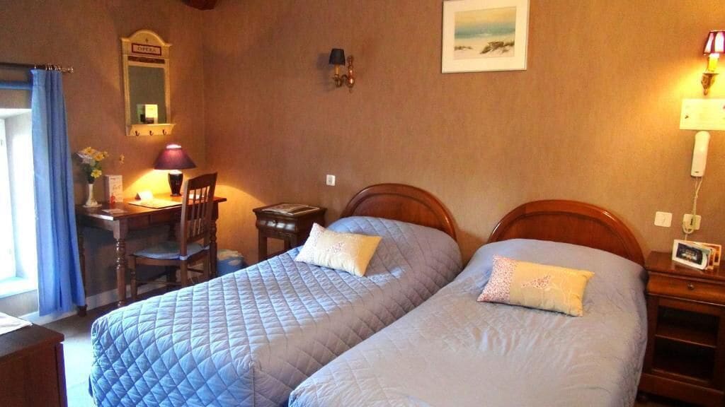 Una habitación con dos camas, un escritorio con silla, un espejo, una lámpara y un cuadro en la pared.