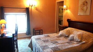 A bedroom with a bed, a desk with a lamp, a chair, and a small stool.