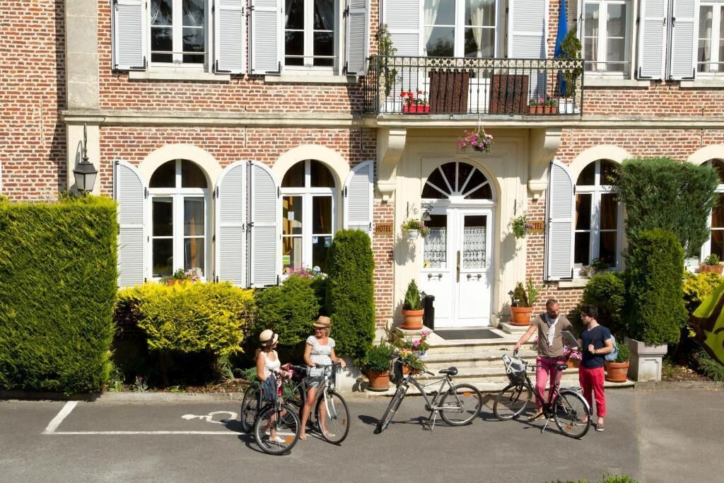 Un hotel con fachada de ladrillo, contraventanas blancas y una entrada central con puerta. Hay bicicletas estacionadas al frente.