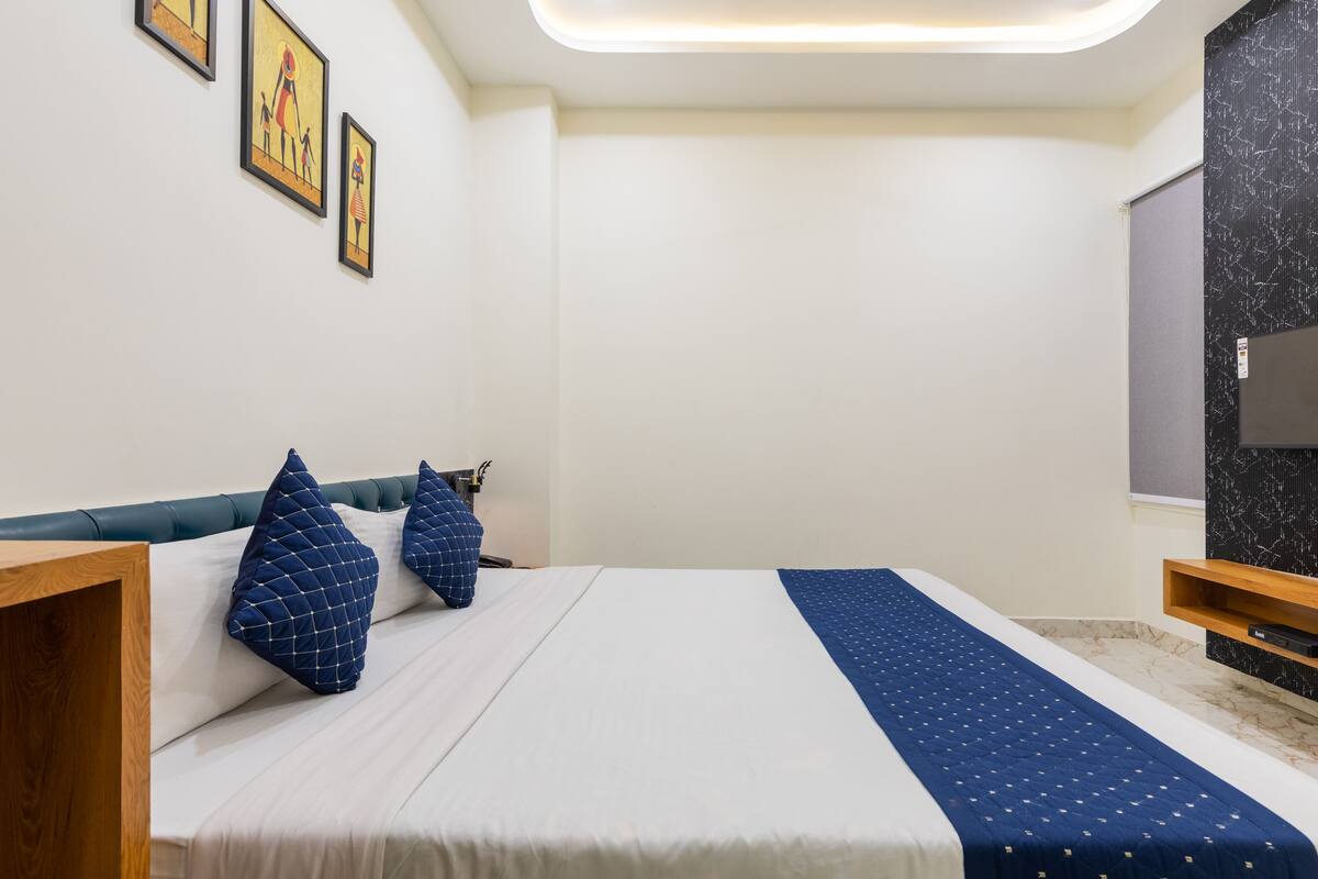 A bedroom with a bed, pillows, a wooden nightstand, a TV, and framed artwork on the wall.