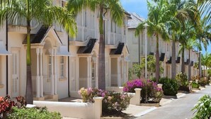 Une rangée de bâtiments de style colonial, peints en blanc et dotés de balcons, entourés de palmiers et de plantes en fleurs.