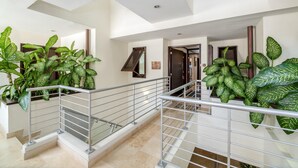 Un hall d’hôtel moderne avec un escalier, des rampes en métal et de grandes plantes vertes.