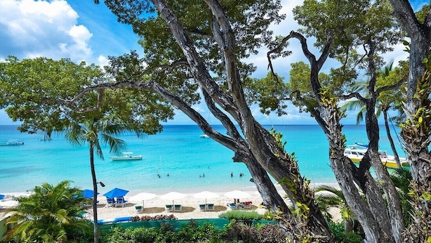 Une plage à l’eau turquoise et limpide, un rivage sablonneux et plusieurs bateaux.