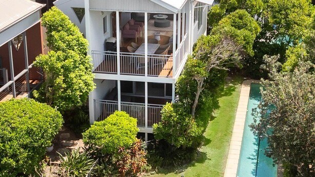 A multi-story house with a swimming pool, surrounded by lush greenery.