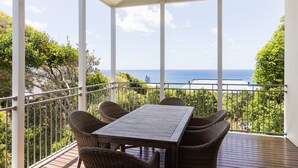 A covered balcony with a table and chairs, overlooking a view of the ocean.