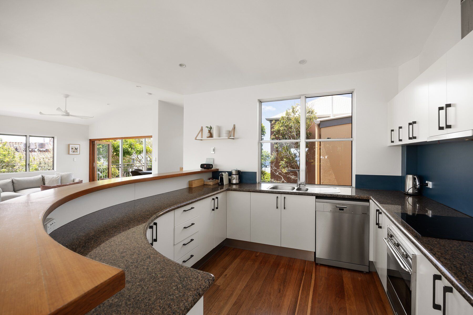 A modern kitchen with a curved countertop, built-in dishwasher, and a large window providing natural light.