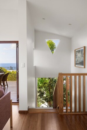 A modern interior with a wooden staircase, a triangular skylight, and a view of greenery outside.