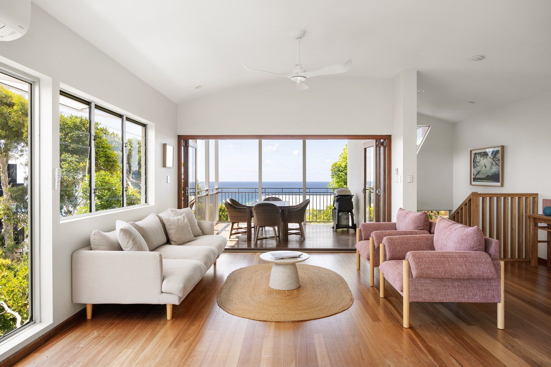 A spacious living room with a large window, a ceiling fan, and a view of the ocean.