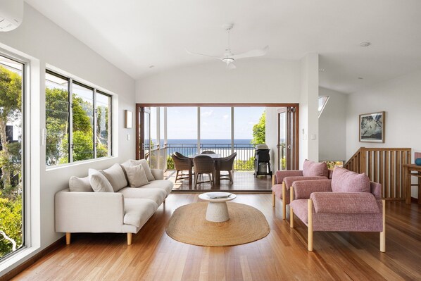 A spacious living room with a large window, a ceiling fan, and a view of the ocean.