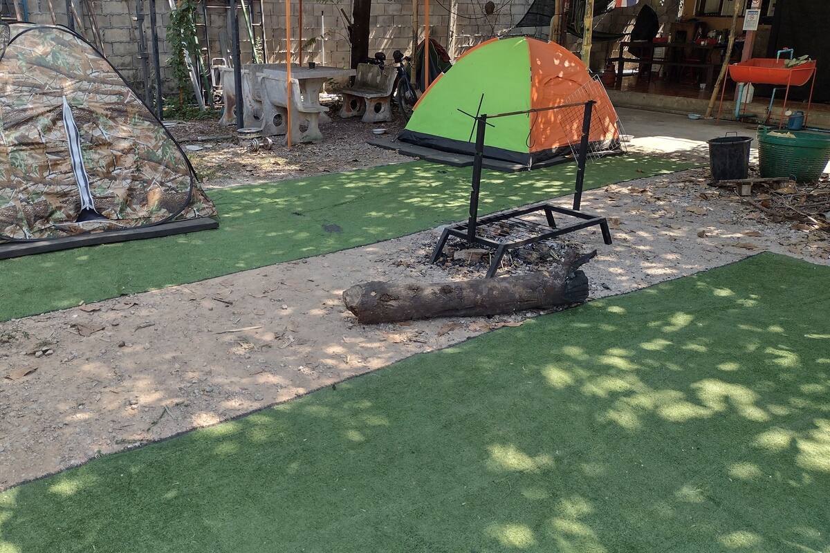 A campsite with two tents, one camouflage and one green and orange, on artificial grass with a dirt path.