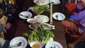 Una larga mesa de comedor con diversos platos y utensilios, rodeada de comensales sentados.