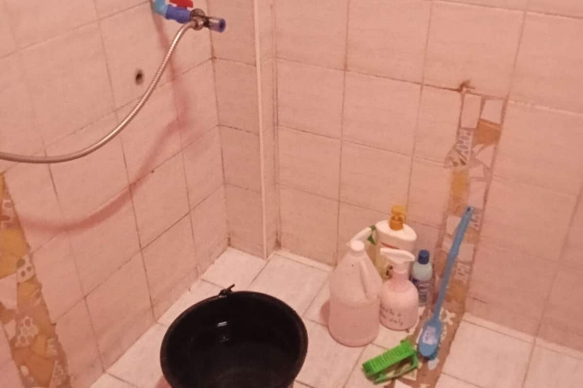 A small bathroom with a shower, a black bucket, and cleaning supplies on the floor.