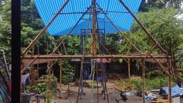 A bamboo structure with a blue tarp roof, surrounded by potted plants and bicycles.