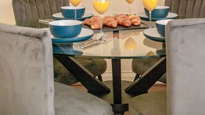 Un coin repas avec une table en verre, quatre chaises et une œuvre d’art abstraite encadrée accrochée au mur.