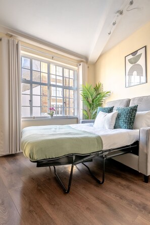 A bedroom with a bed, a window with curtains, a plant, and a painting on the wall. - Charming 1BR in London's Westminster (London)