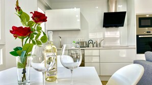 A dining table with a bottle of wine, two wine glasses, and a vase with roses.