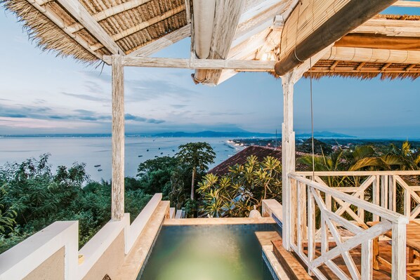 A wooden deck with a pool overlooking a coastal area.