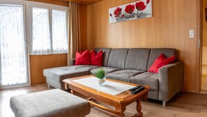A modern living room with a grey sectional sofa, red cushions, a wooden coffee table, and a grey ottoman.