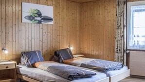 A wooden-paneled room with two beds, a nightstand, a window with curtains, and a wall-mounted light.