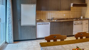 A modern kitchen with dark wooden cabinets, a white refrigerator, a built-in dishwasher, and a stove.