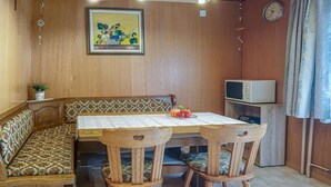 A dining area with a wooden table, four chairs, a bench, a clock, and a television.