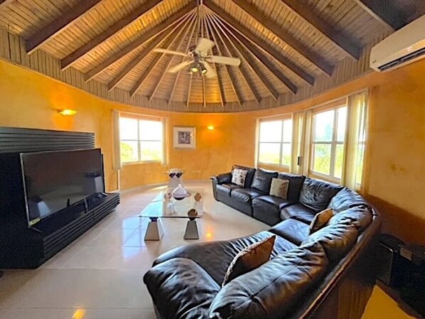 A spacious living room with a large sectional sofa, a flat-screen TV, and a ceiling fan.